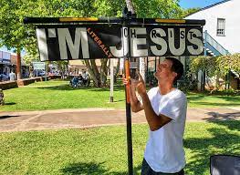 This is a picture of A man in Banyan Park,, Maui, HI With A Cross That says, I Am Literally Jesus